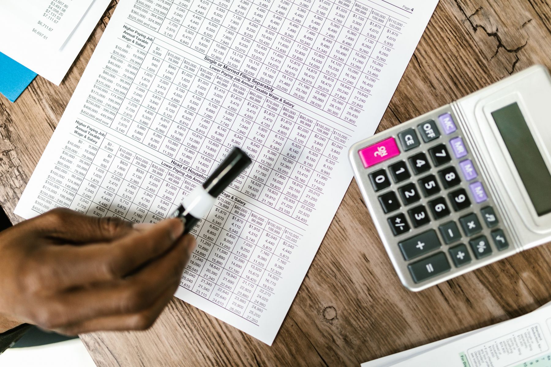 Hand marking figures on a printed ledger beside a calculator